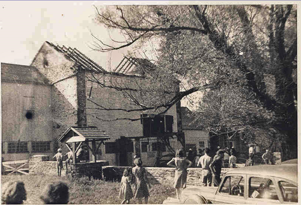Black and white photo shows a crowd gathered to see the barn damaged by fire