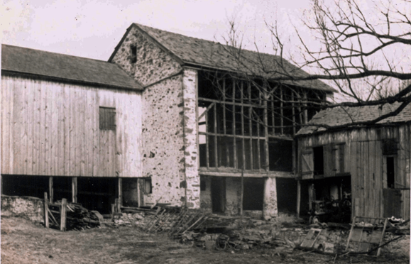 black and white photo shows a barn with all siding removed, revealing the wooden stud framing