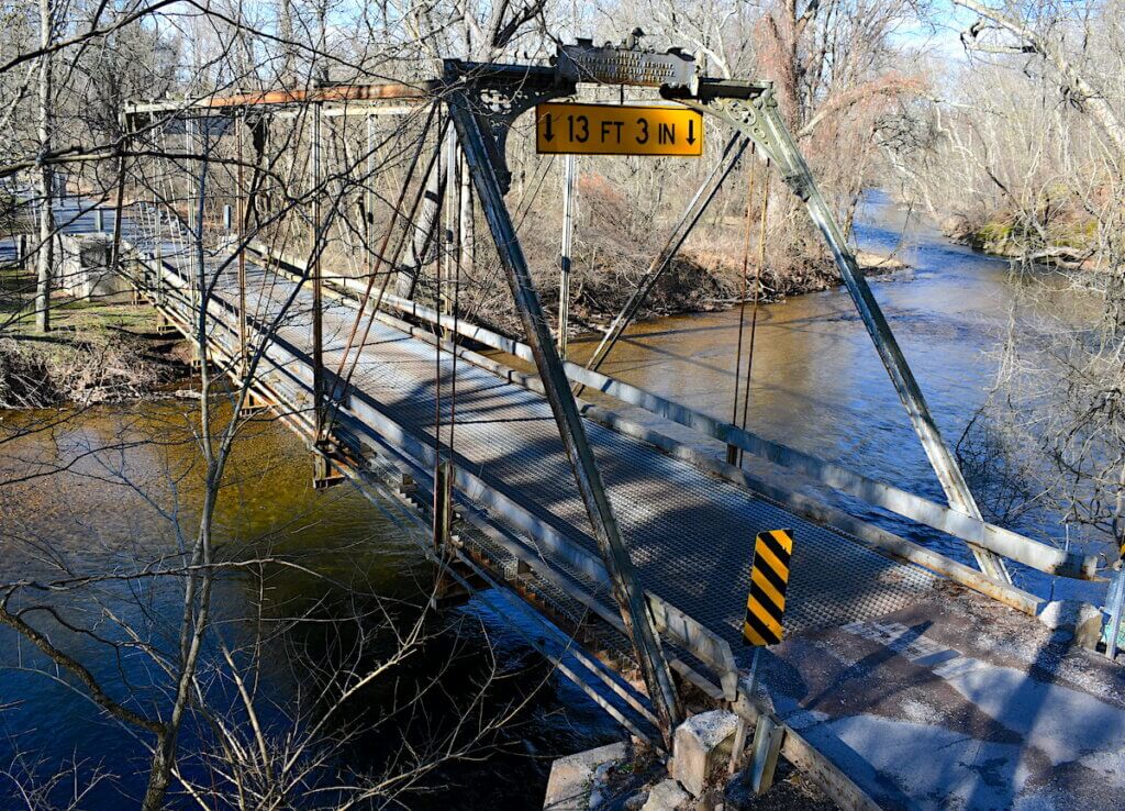 A drone's-eye view of a metal truss bridge over a creek.