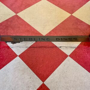 Red and white diamond-shaped floor tiles frame a metal plate that says "Sterling Diner"
