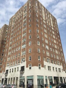 A brick and limestone Art Deco highrise building features retail at the ground level and apartments above