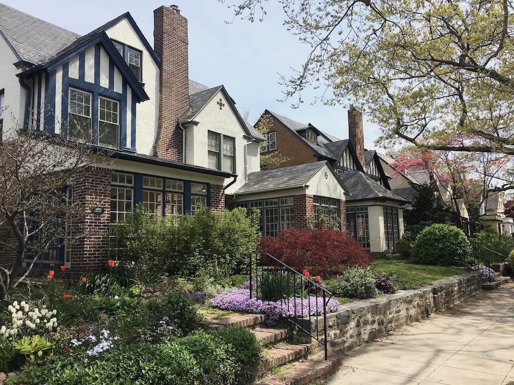 Garden Court neighborhood homes feature glass in entryways, tall chimneys and tudor-like styling, a front garden with a low stone wall along the edge of the sidewalk