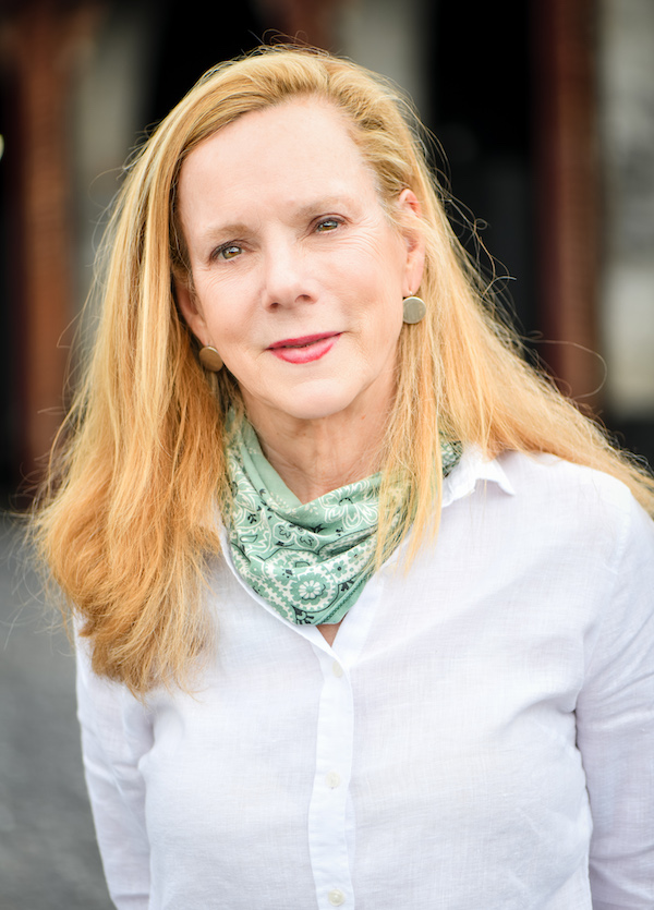 a woman looks at the camera, wearing a blue shirt and a green kerchief