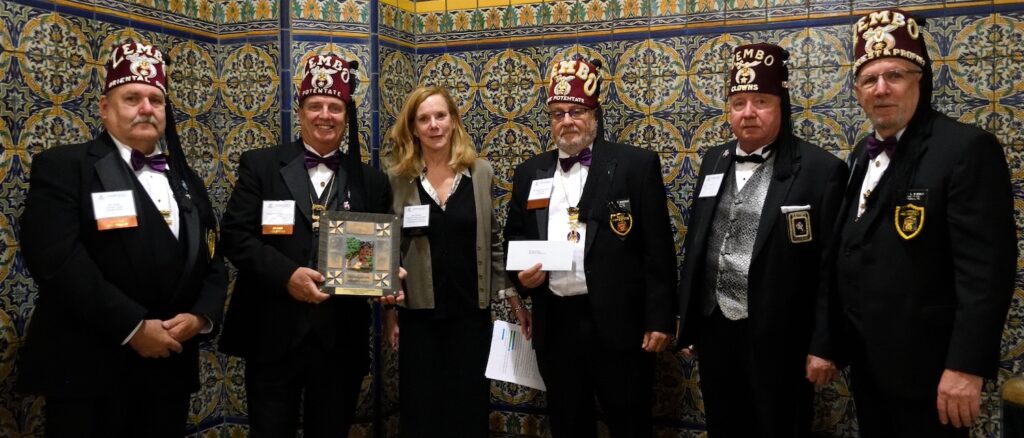 Jane Sheffield presenting a tile award plaque to Zembo Shriners in fez hats against a decorative tile wall